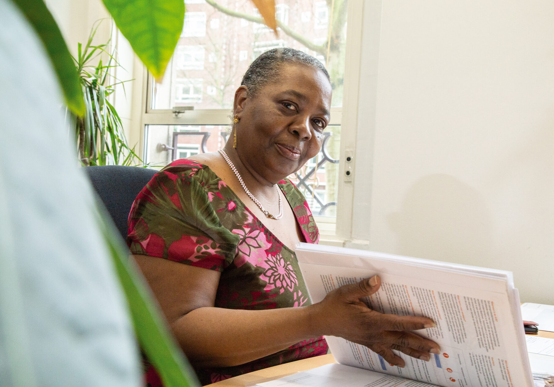 IMG_3036 Op deze foto is een dame te zien die een opengeslagen map vasthoudt. De vrouw kijkt in de camera en draagt een gebloemde blouse.